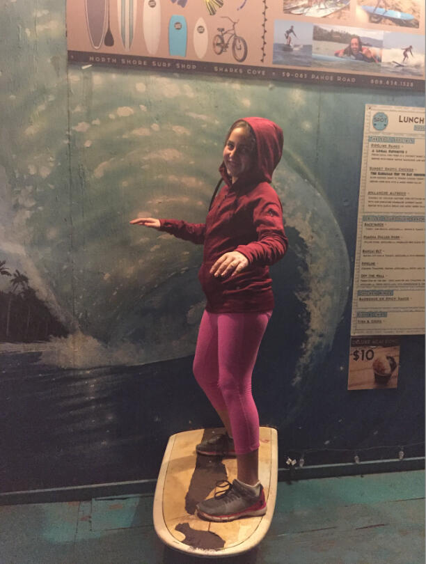 Emily Mitnick on a surfboard installed in surfing theme restaurant with surfing inspired menu on the background.